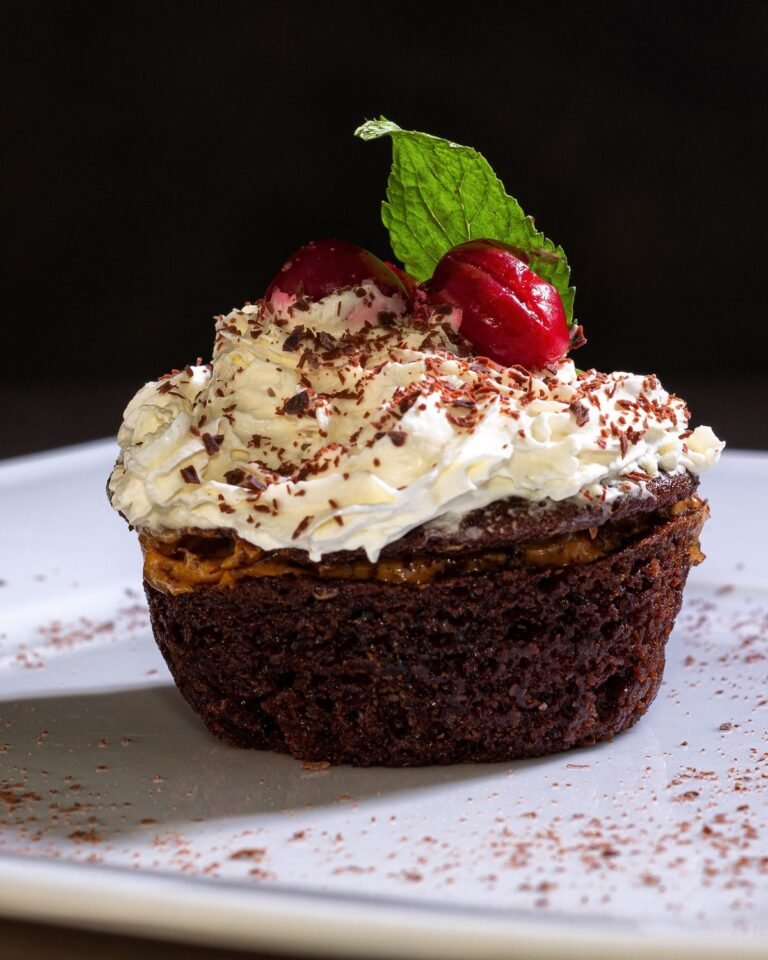 Chocolate cupcake topped with whipped cream, cherries, and chocolate shavings