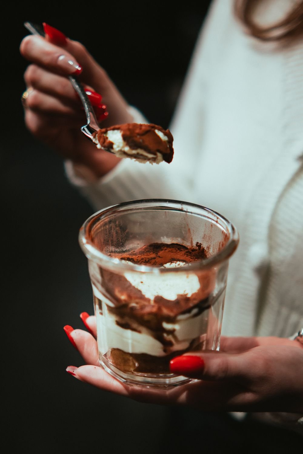 A spoon lifting a bite of cocoa-dusted chai spiced tiramisu, showing creamy mascarpone and soaked sponge layers.