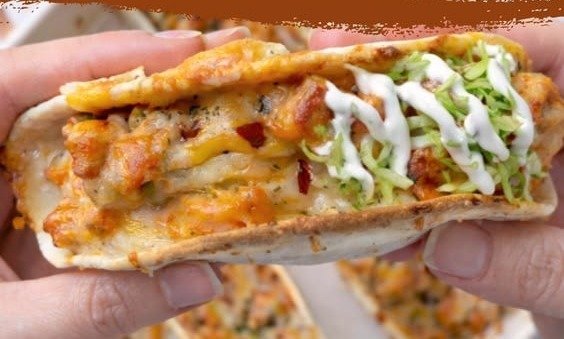 Cheesy chicken bacon ranch taco held in hand with ranch drizzle and shredded lettuce