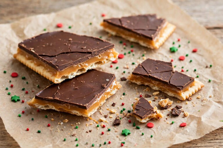 Broken pieces of Christmas crack saltine toffee with a chocolate layer and chopped pecans on top, stacked on a plate for a holiday dessert tray.