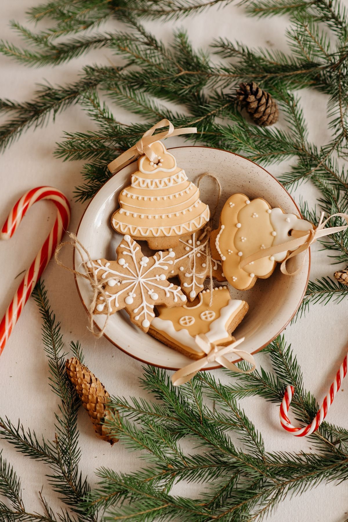 Classic gingerbread cookies in holiday shapes with light icing details, arranged on a wooden surface with pine branches and warm festive decorations.