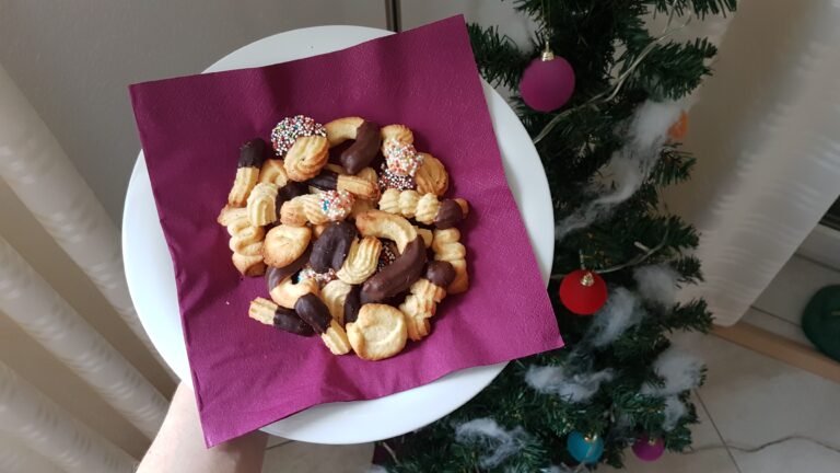 Classic spritz cookies, piped butter spritz in ridged shapes, some dipped in chocolate, held beside a Christmas tree