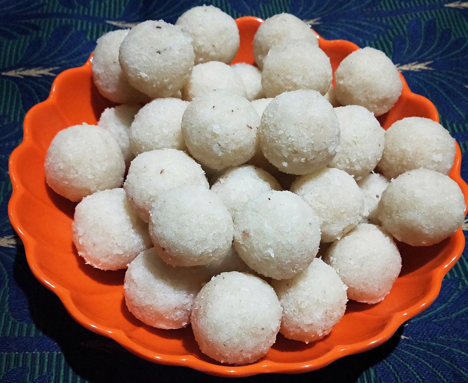 A bright orange plate piled high with round white coconut ladoo balls coated in shredded coconut, ready to serve.