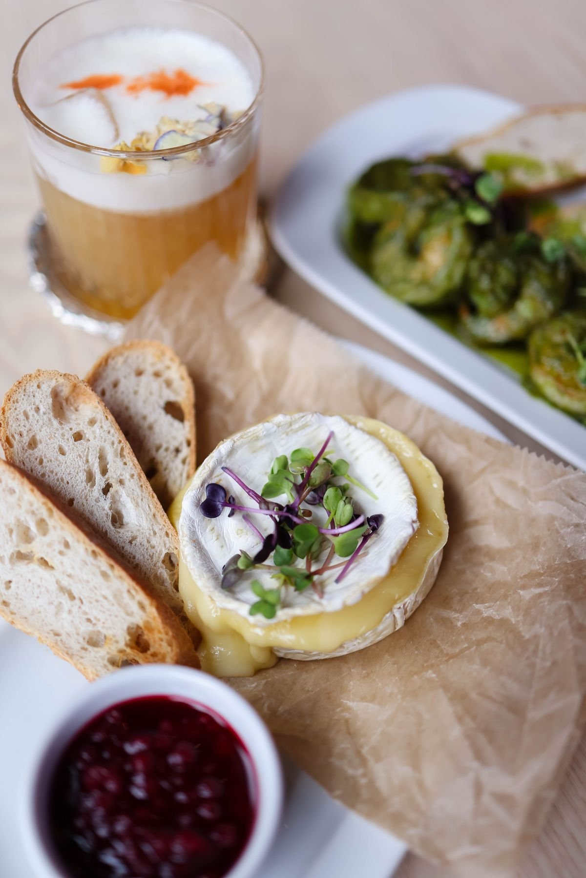 Baked brie wheel served with sourdough bread and a bowl of cranberry sauce.