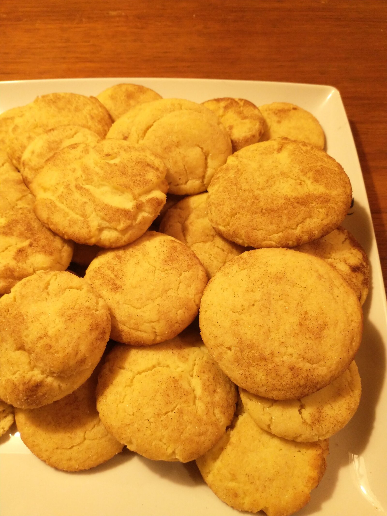 Eggnog Snickerdoodles (Soft, Cinnamon-Sugar, With Real Eggnog) 2 A white platter piled high with round golden cinnamon-sugar-coated snickerdoodle cookies on a wooden table