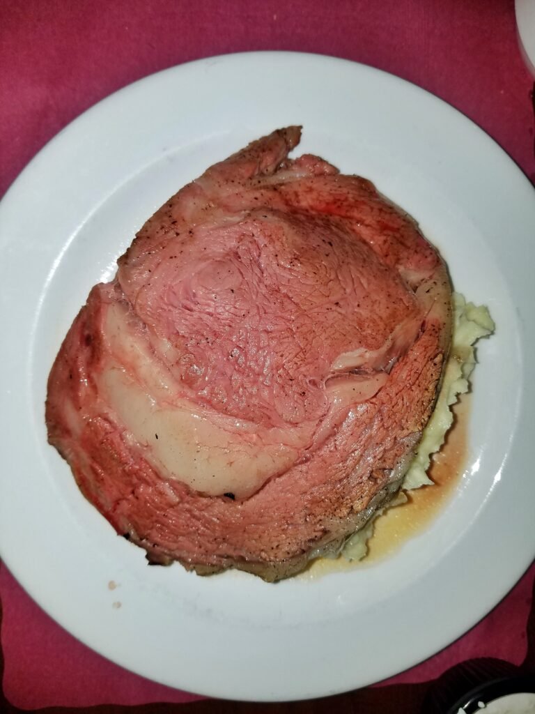 A thick slice of pink-centered prime rib roast served on a white plate with mashed potatoes
