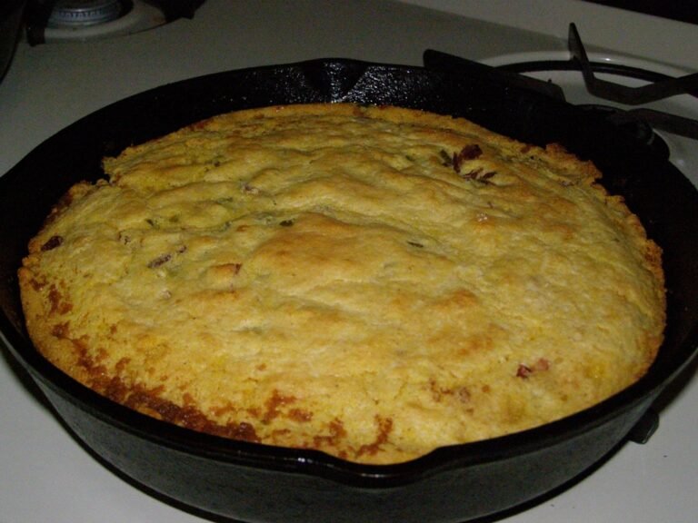A golden skillet cornbread with flecks of green chile and jalapeño baked in a black cast-iron skillet on a stovetop.