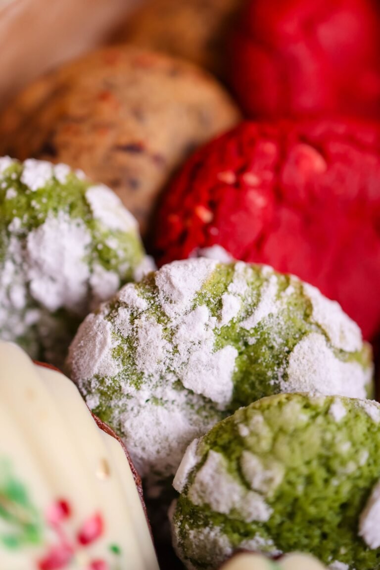 Close-up of bright green crinkle cookies dusted with powdered sugar, with red cookies beside them in a holiday cookie box