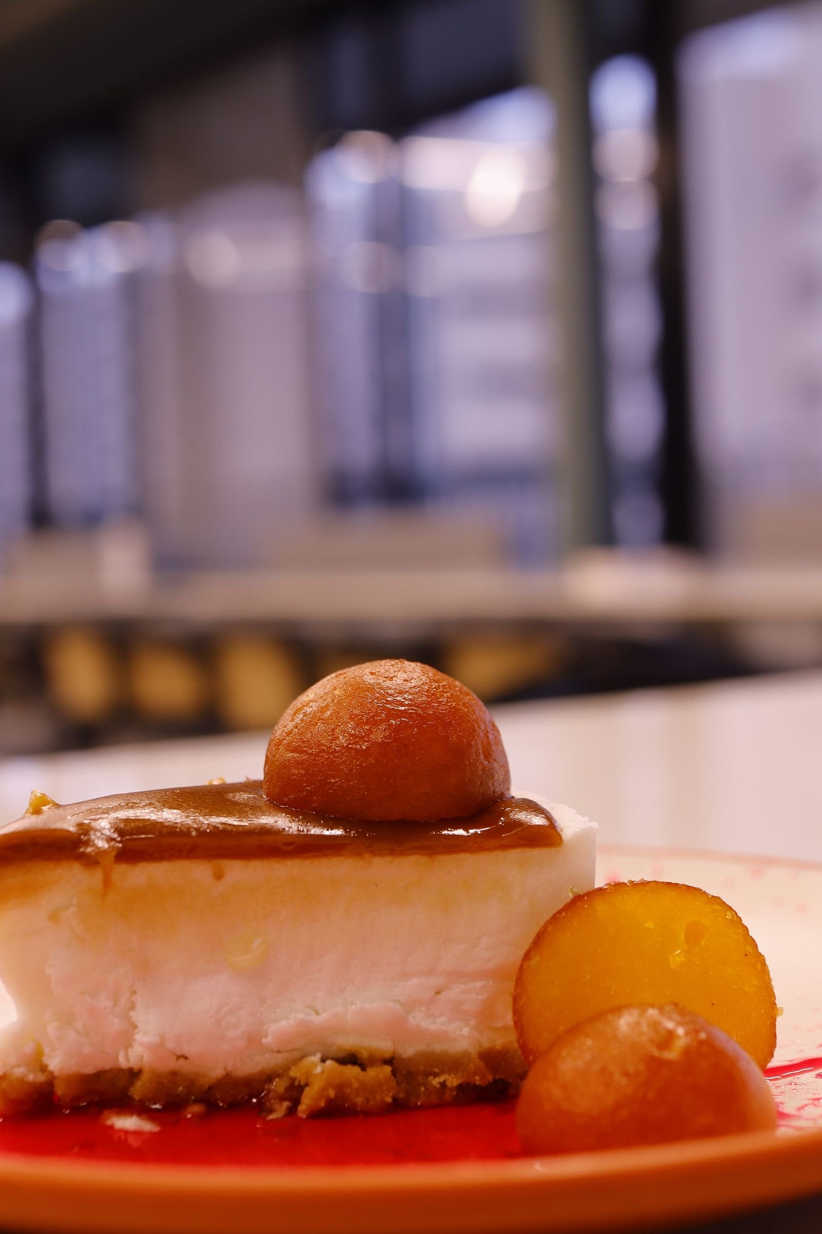 Gulab Jamun Cheesecake (No-Bake, Cardamom, Rose, Ready in 6 Hours 25 Minutes) 2 A slice of creamy white cheesecake with a biscuit base, topped with a whole golden gulab jamun and syrup, with more gulab jamuns beside it