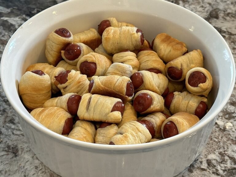 Golden Halloween mummy hot dogs wrapped in crescent dough with candy eyes on a serving platter