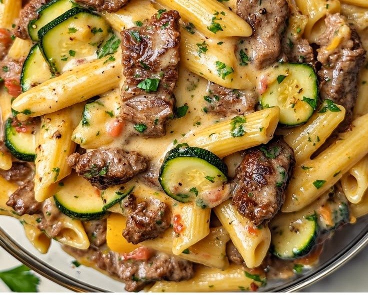 Healthy creamy steak penne with zucchini, cherry tomatoes and fresh parsley in a glass bowl