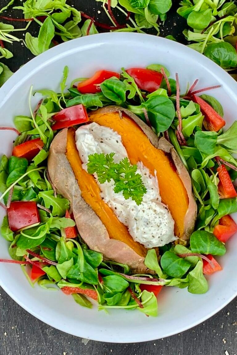 Baked sweet potato split open and stuffed with creamy cheese filling on a salad bowl