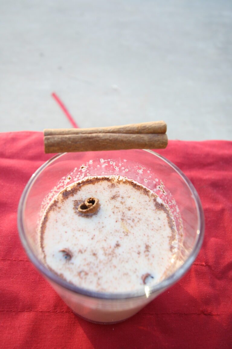 A glass of creamy homemade eggnog dusted with cinnamon and nutmeg beside cinnamon sticks