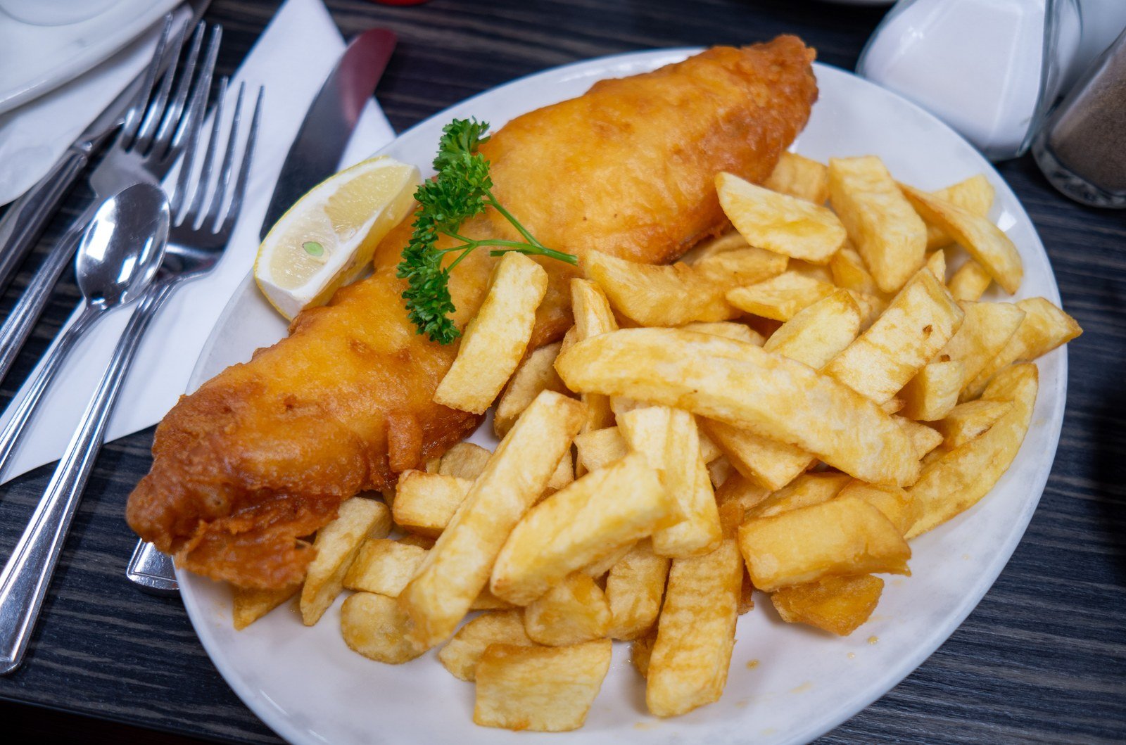 Golden crispy beer-battered fish fillet with thick-cut chips, lemon wedge and parsley