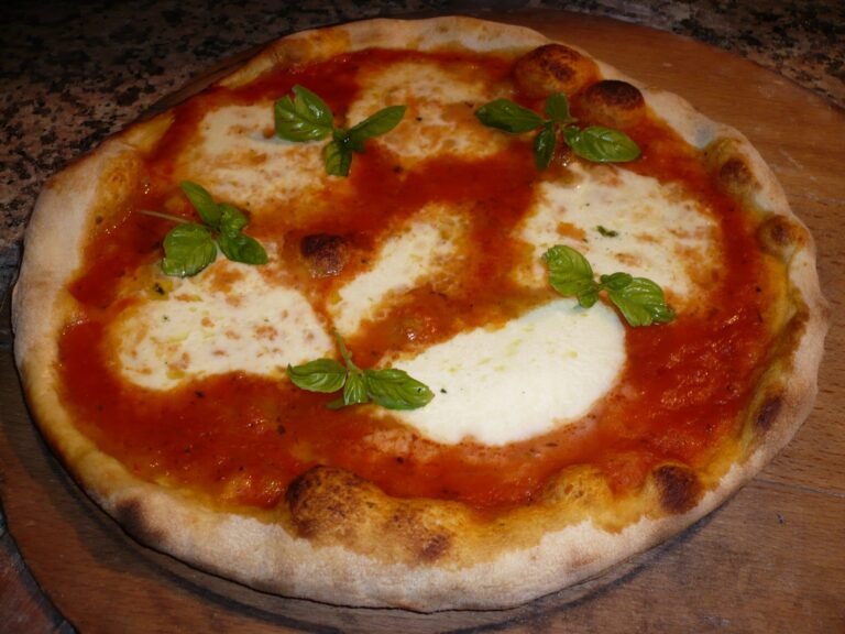 A whole homemade margherita pizza with tomato sauce, melted mozzarella pools and fresh basil on a wooden board