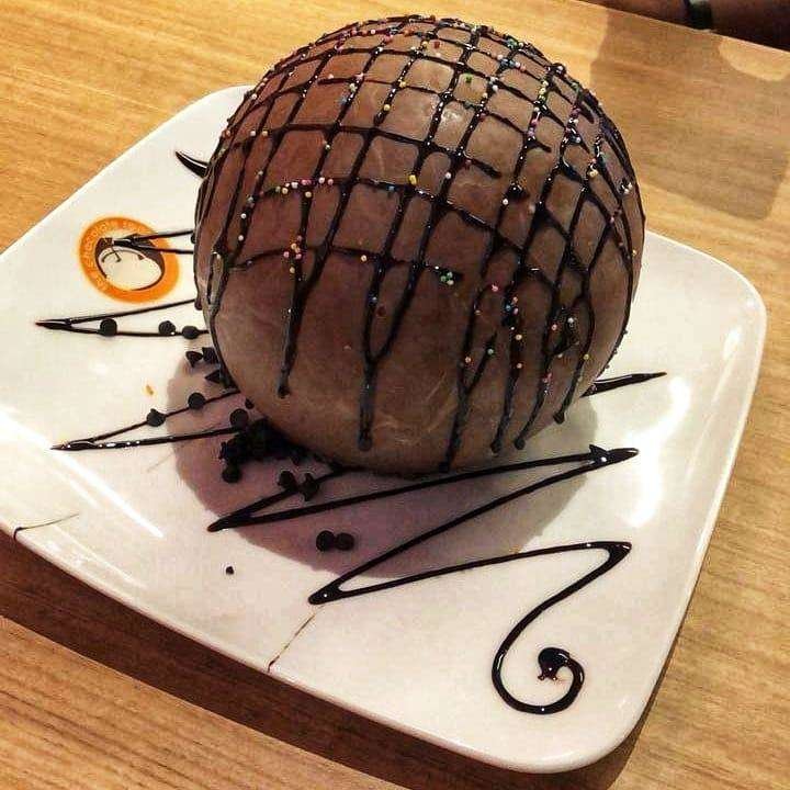 A single large milk chocolate bomb with drizzle and sprinkles on a plate.