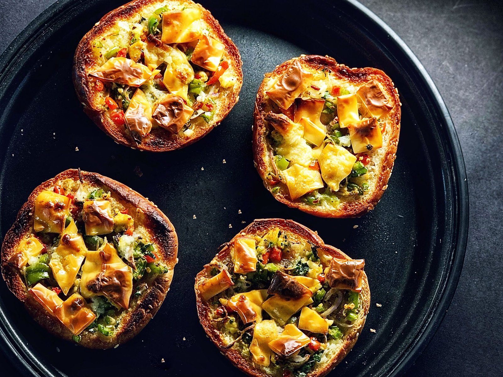 Four small bread pizzas with melted cheese squares on a black tray, top-down view