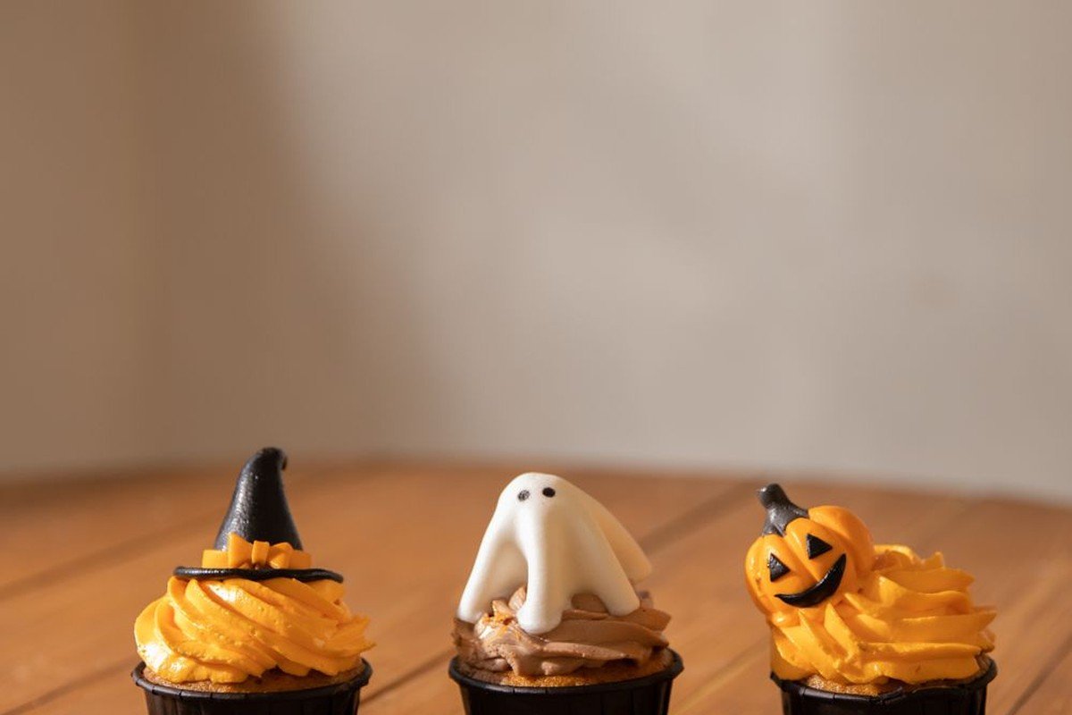 Three mini Halloween cupcakes — witch hat, ghost and jack-o'-lantern on wood