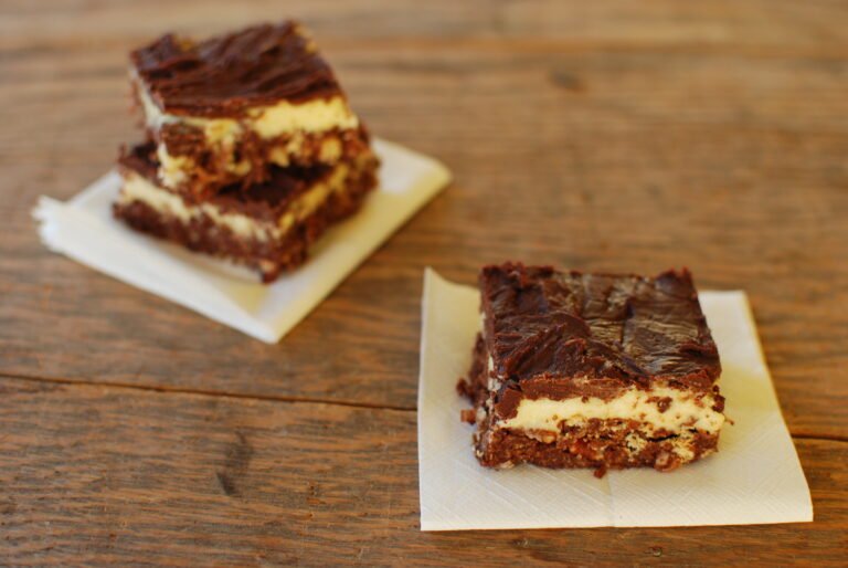 Stacked Nanaimo bars showing the chocolate crumb base, pale custard middle and glossy chocolate top