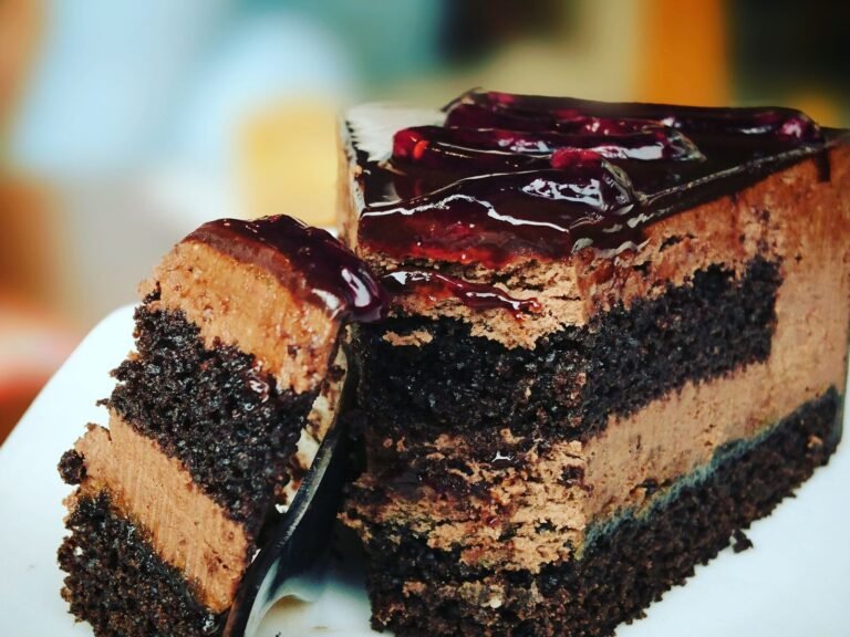 Moist one-bowl chocolate fudge cake slice with glossy ganache on a plate