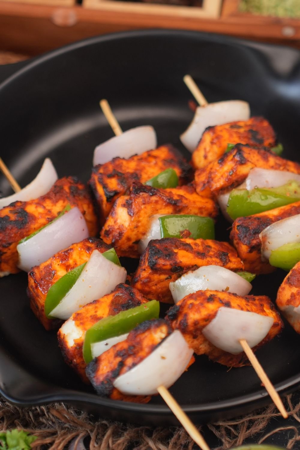 Charred paneer tikka skewers with green peppers and onion pieces arranged in a black serving dish, ready to serve