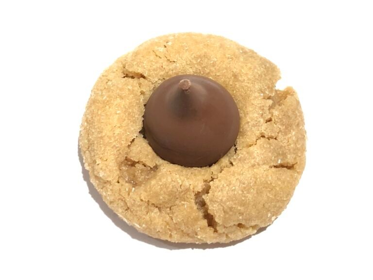 A plate of soft peanut butter blossom cookies rolled in sugar, each topped with a chocolate kiss pressed into the center of the cookie.