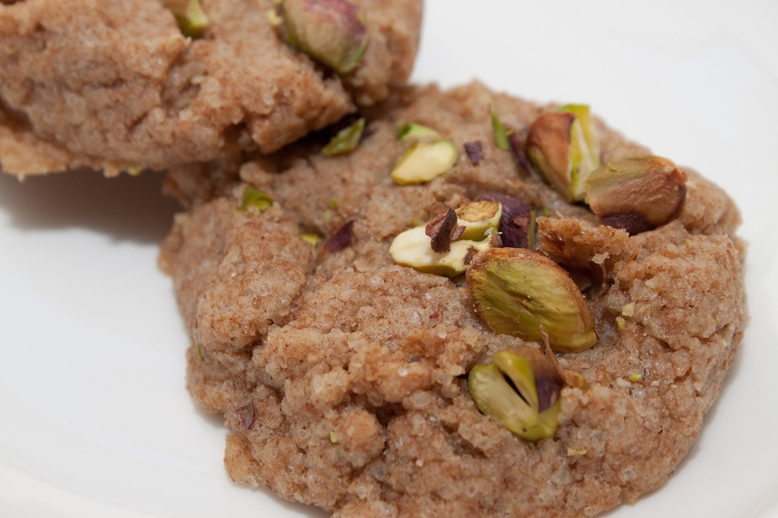 Pistachio Rose Shortbread (Buttery, Crumbly, With Rosewater) 2 Crumbly pistachio shortbread rounds topped with chopped pistachios and dried rose petals on a white plate