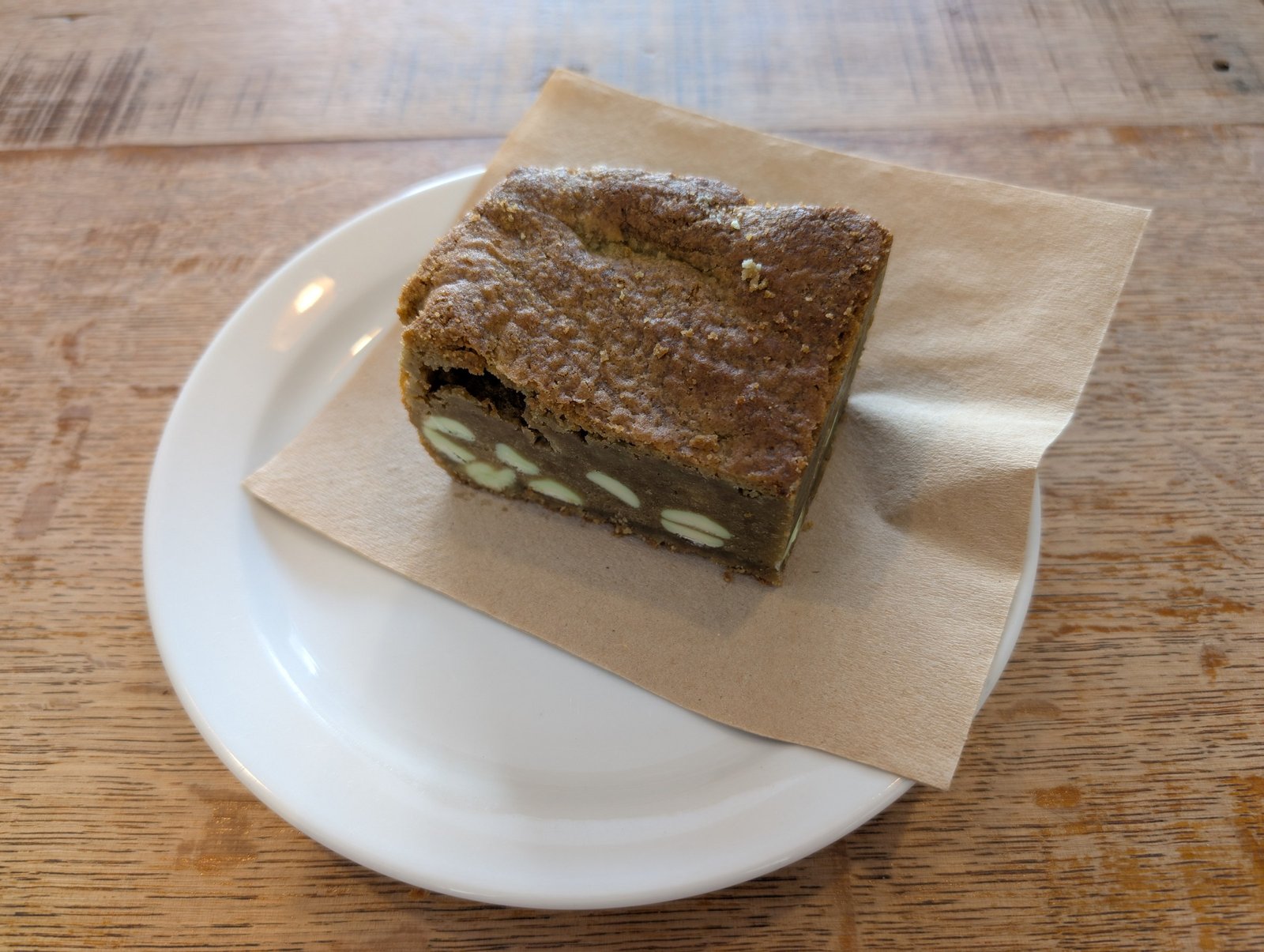 A square pistachio blondie with green pistachio pieces visible in the golden crumb, served on a white plate