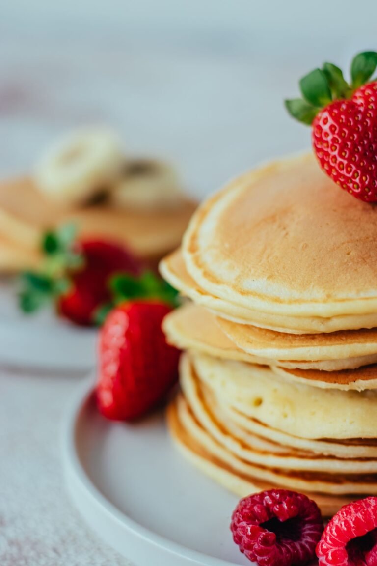 Stack of thick, golden protein pancakes topped with strawberries and raspberries