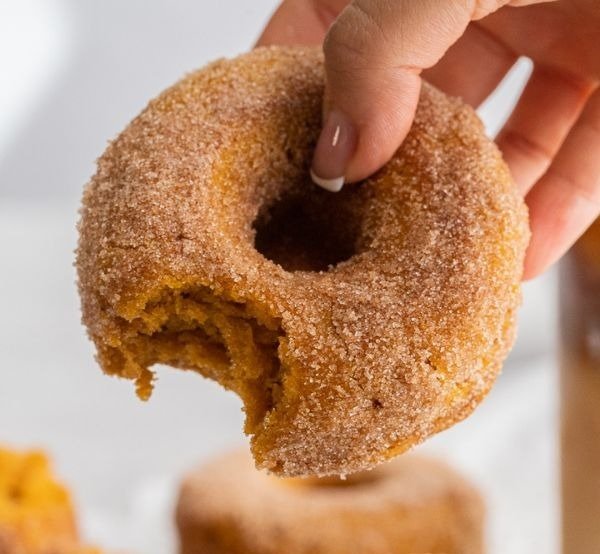 Pumpkin spice baked donuts coated in cinnamon sugar, one held with a bite taken out