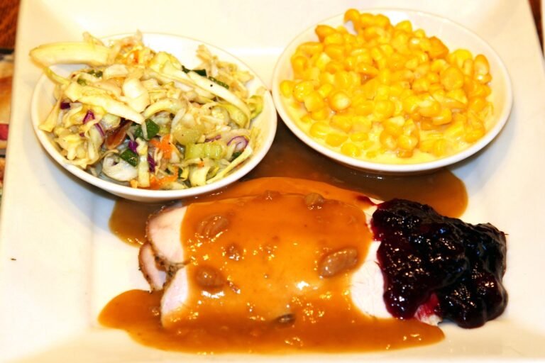 Sliced roast turkey breast covered in glossy brown gravy with cranberry sauce, served on a white plate with sides
