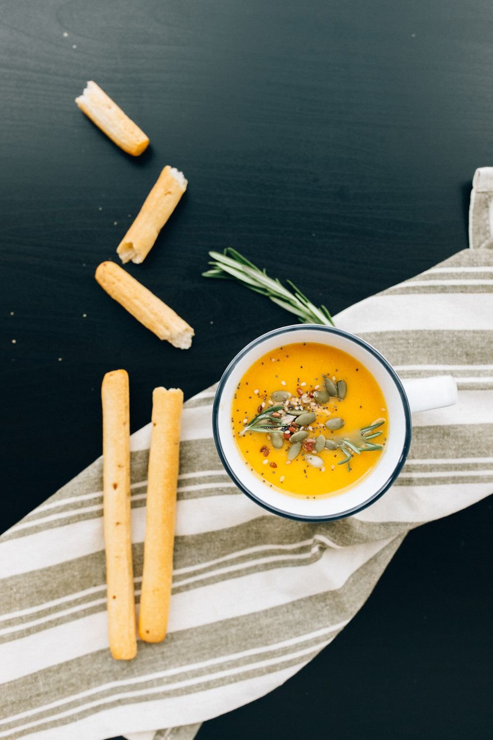 A mug of roasted butternut squash soup with breadsticks, a second angle of the same dish.