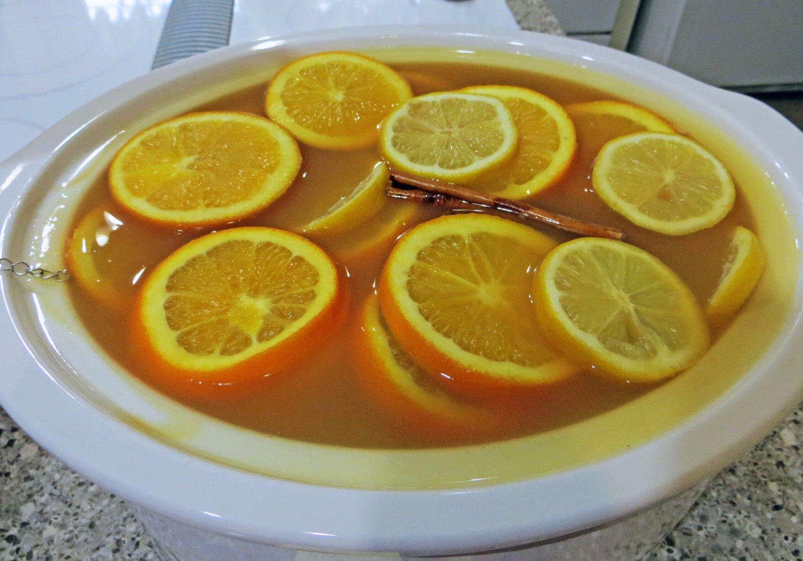 Slow-Cooker Christmas Wassail (Warm Spiced Cider for a Crowd) 2 A white slow cooker crock filled with warm amber Christmas wassail, garnished with orange slices, lemon slices, and a cinnamon stick