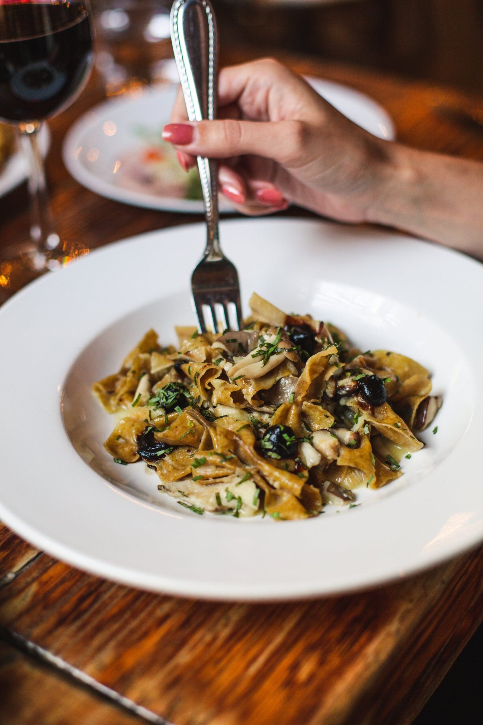 Soy Butter Mushroom Pasta (Japanese Wafu Spaghetti, 30 Minutes) 3 Mushroom pasta with wide ribbon pasta, dark olives, and herbs in a white bowl, a hand holding a fork