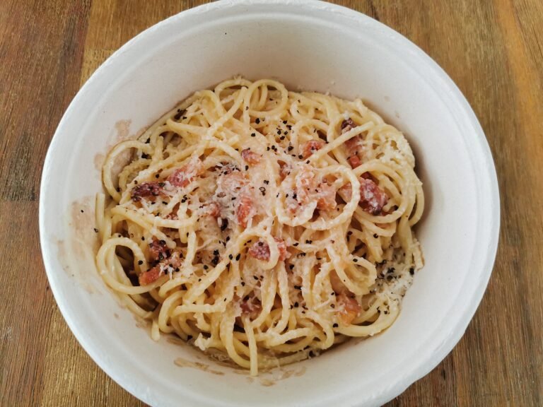 A white bowl of spaghetti carbonara with creamy egg and cheese sauce, crispy guanciale, grated cheese, and cracked black pepper on top