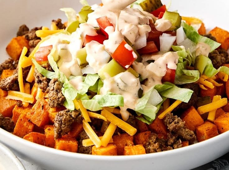Sweet potato burger bowl with seasoned beef, lettuce, tomato, cheddar and creamy burger sauce