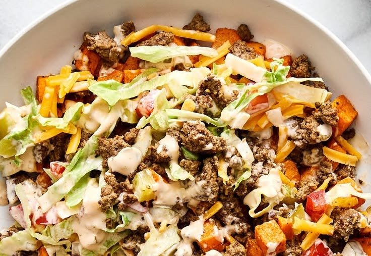 Burger bowl over roasted sweet potato cubes with fresh toppings and burger sauce