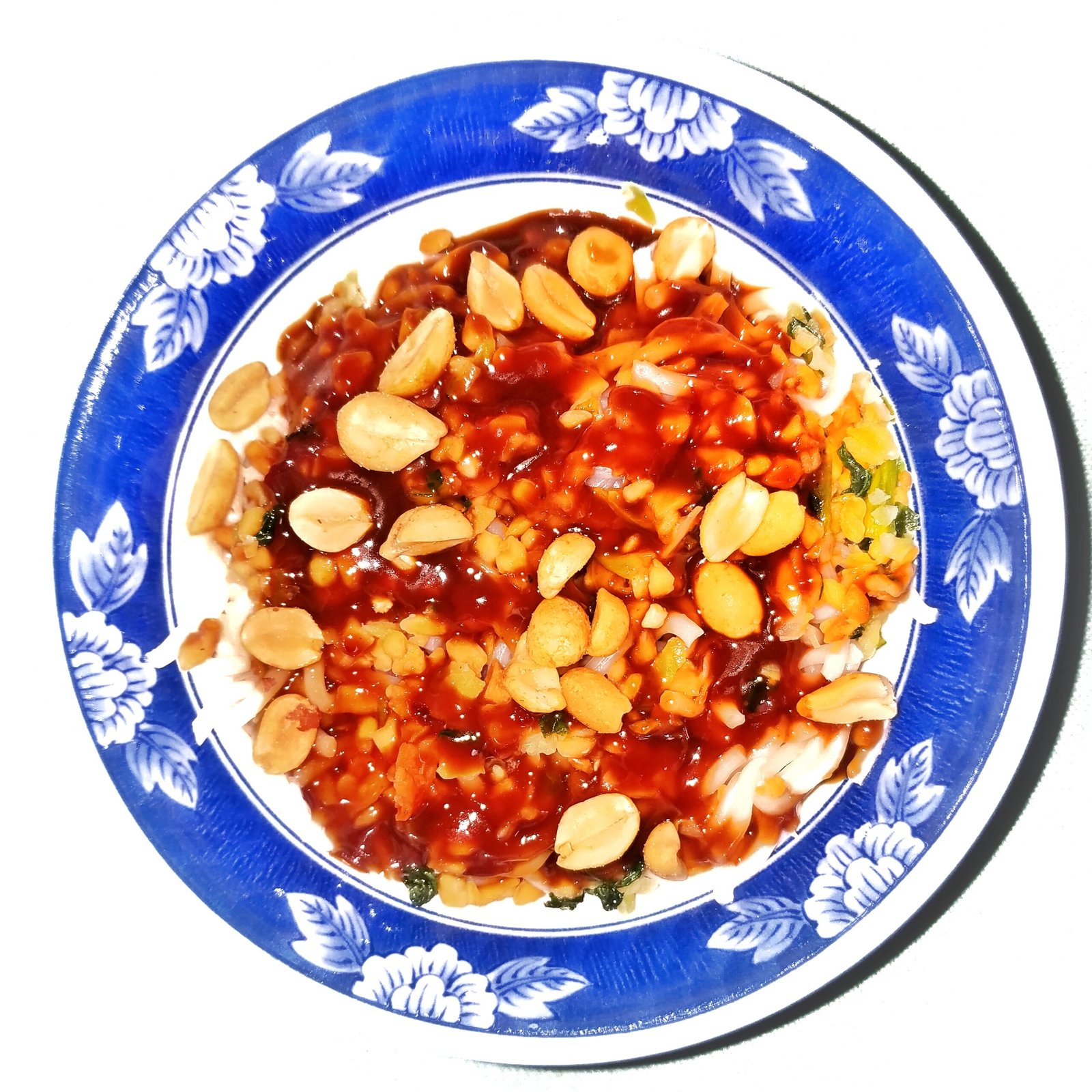 Thai Peanut Chili Noodles (30-Minute, Saucy, Boldly Spiced) 2 A plate of Thai peanut chili noodles topped with whole peanuts and glossy red chili peanut sauce in a blue patterned bowl.